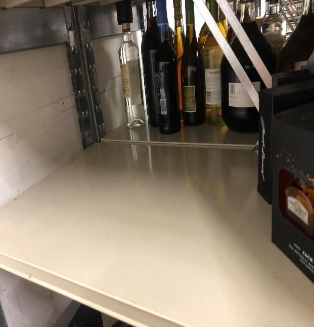 Shelves with bottles of liquor, mostly dark glass, with empty space in front.
