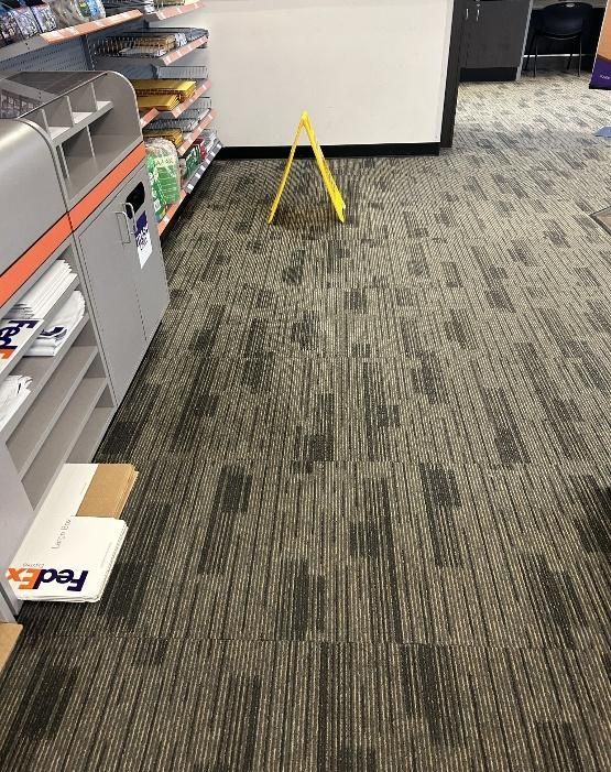 Yellow wet floor sign on patterned carpet in a store.