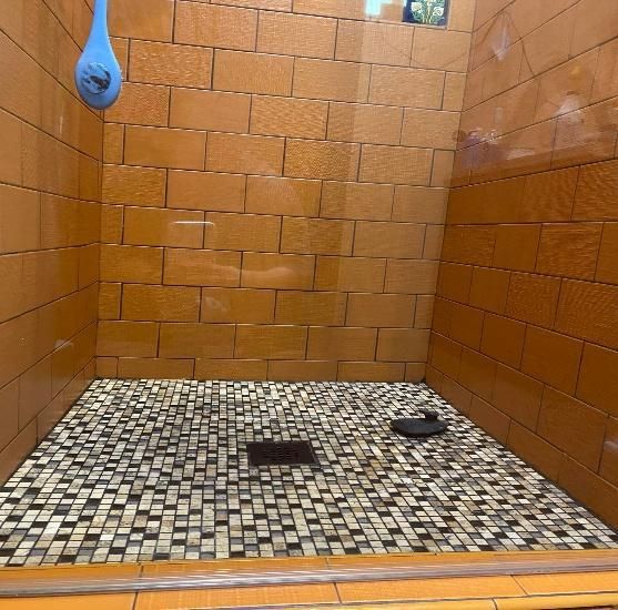 Shower stall with orange tiled walls, mosaic floor, and a blue shower head.
