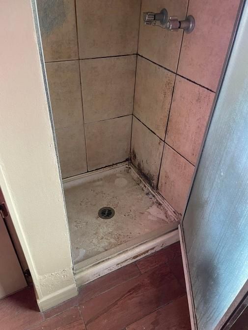 Shower stall with dirty, stained tiles and a buildup of grime.