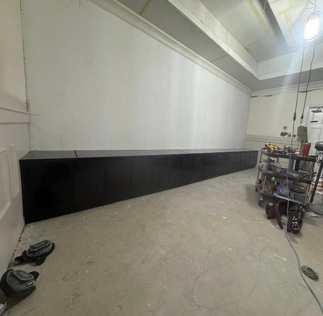 Black baseboard painted on a white wall in a room with concrete floor and a tool cart.