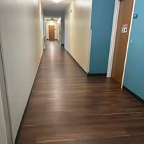 Long, narrow hallway with dark wood flooring, white and turquoise walls, and a door at the end.