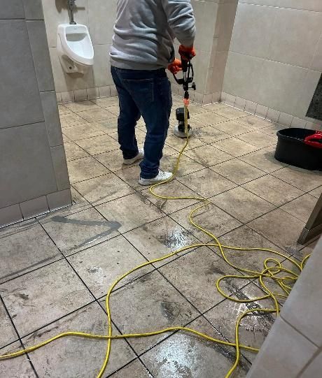 Person cleaning a tiled bathroom floor with a power tool, yellow extension cord present.