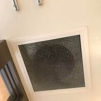 White square air vent in a white ceiling with a dark metallic grid.