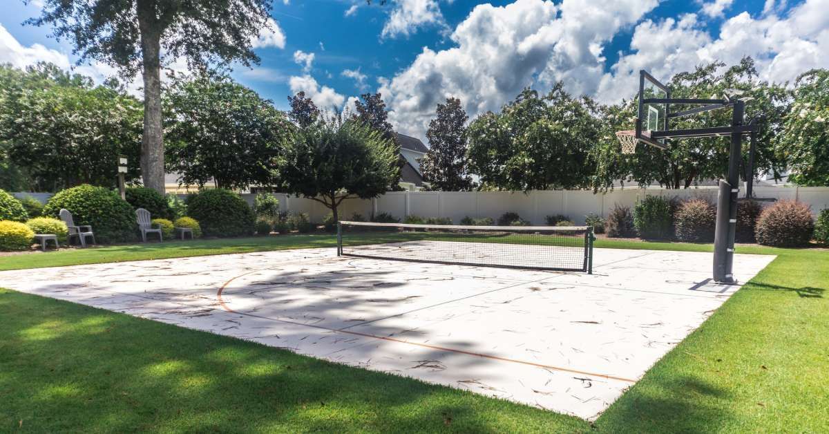 A large backyard home sports court with a tennis net at the center and an adjustable height basketball hoop.