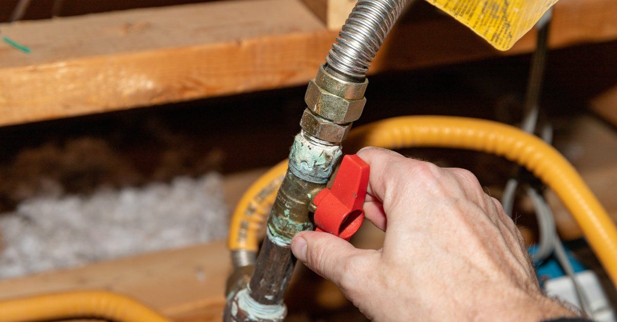 A hand adjusts a red valve on a corroded metal pipe with a flexible connector and yellow tubing in a wooden framework.