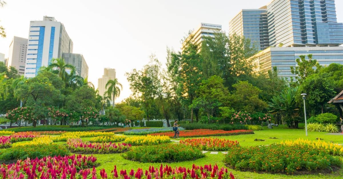 A park with colorful flower beds, green trees, and tall commercial buildings in the background durin