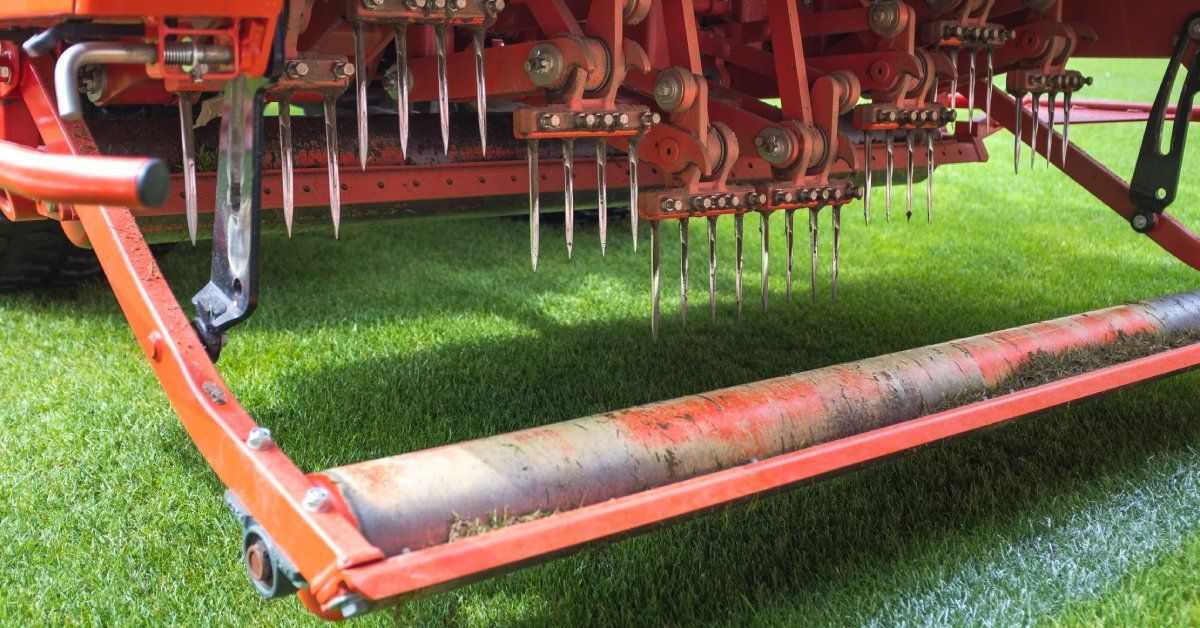 A commercial turf aerator rolling across a turf field. The aerator is red and the spikes are about 4 inches long.