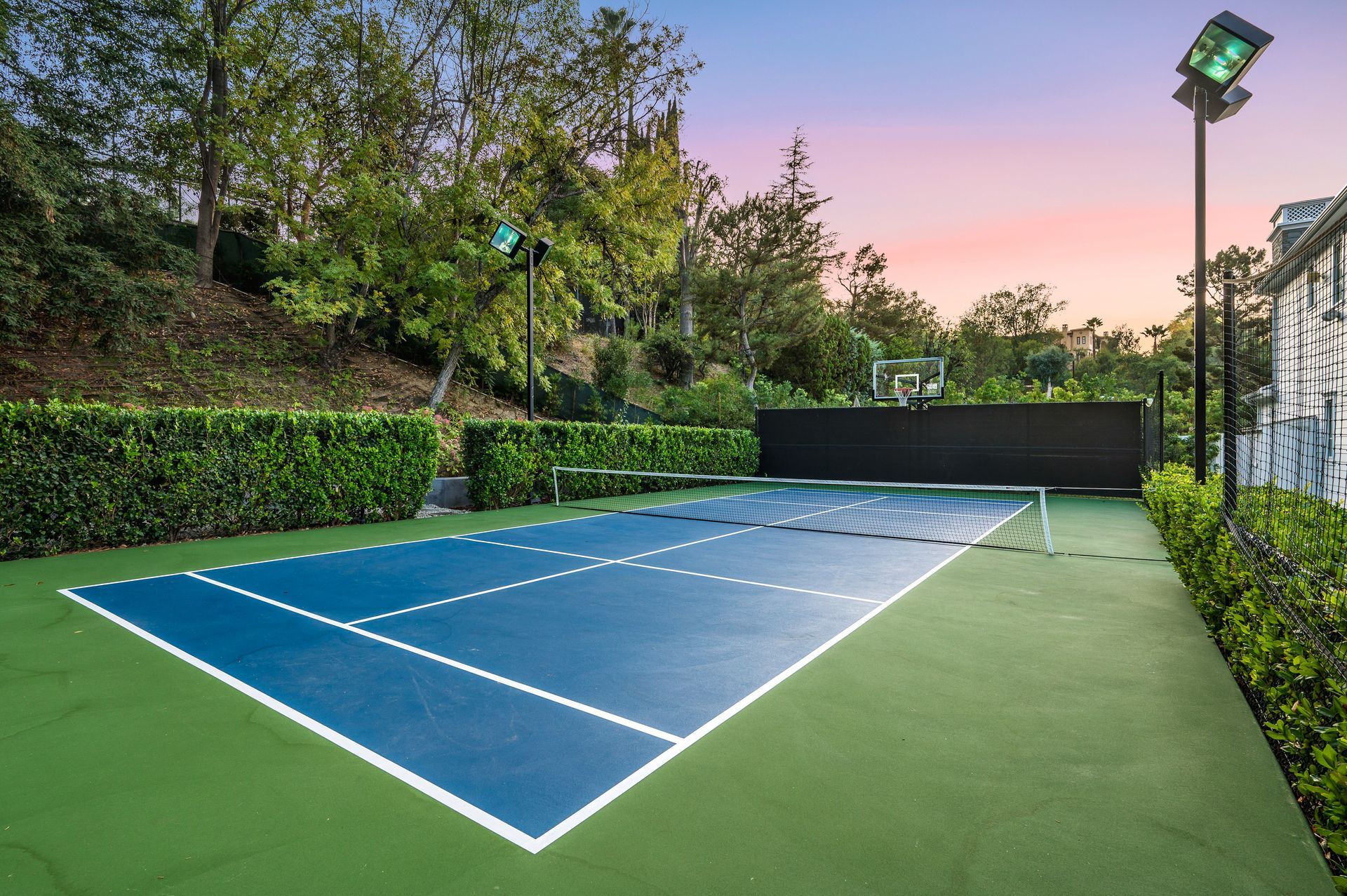 A residential sports court with a blue painted basketball court. There's also a tennis net in the middle of the court.