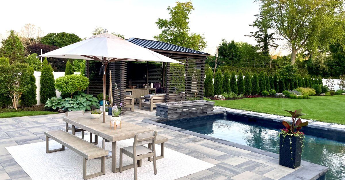 An upscale backyard with an in-ground pool, covered pergola, and a dining table set. 