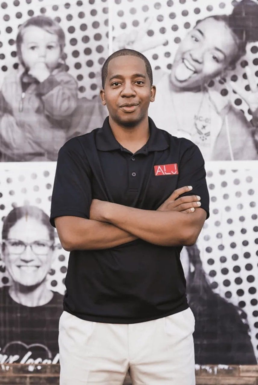 A man with his arms crossed is standing in front of a wall with pictures of people on it.