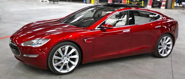 Red Tesla sports sedan in a garage, shown from the side.