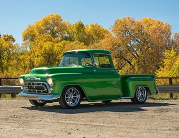 Green classic pickup truck parked outdoors with autumn trees in the background