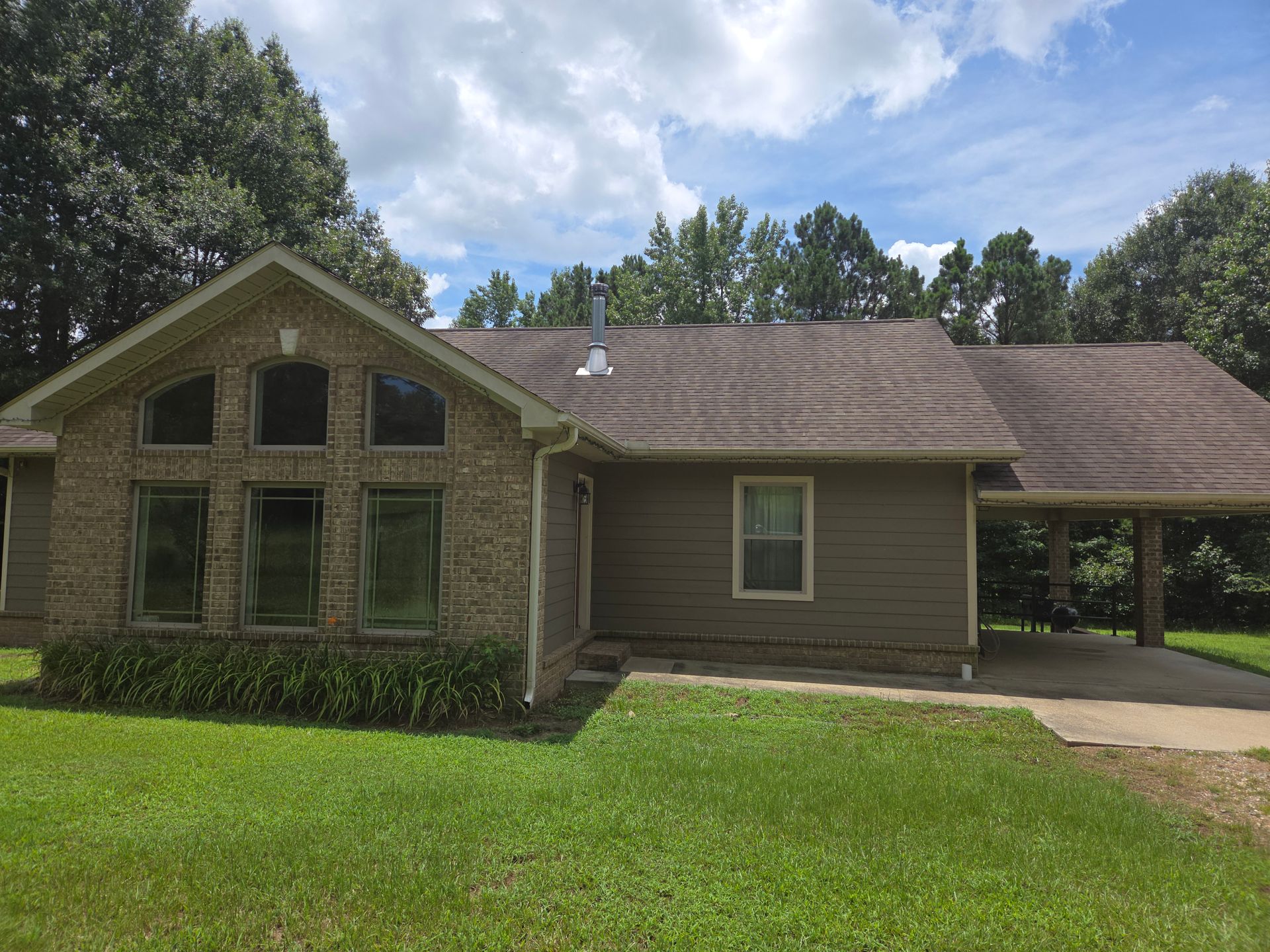 A large brick house with a brown roof is sitting on top of a lush green field.