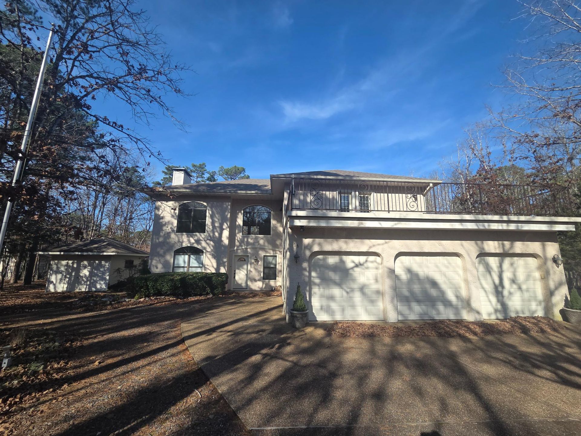 Two-story beige house with attached garage, trees, and blue sky.