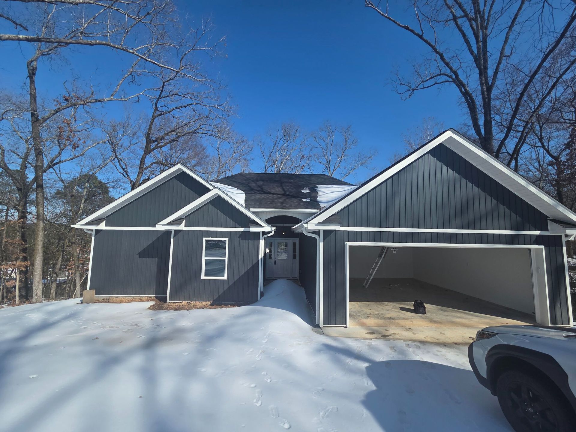 Blue house with attached garage, in a snowy setting with bare trees.