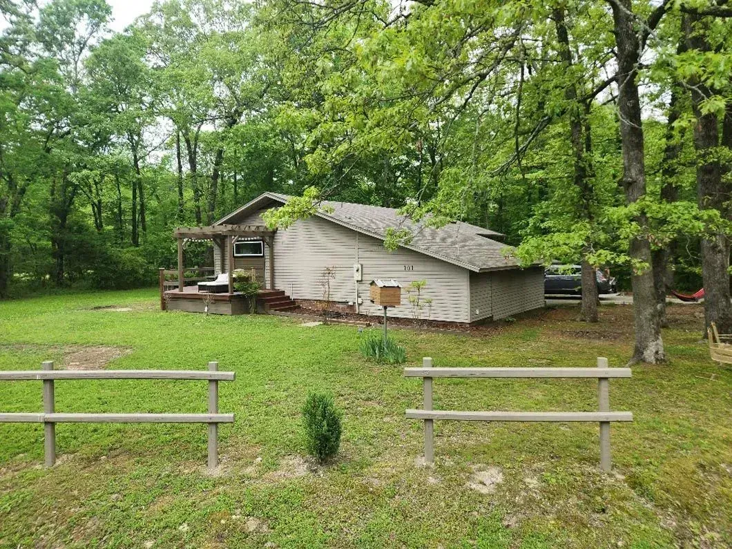 A small house is sitting in the middle of a lush green field surrounded by trees.