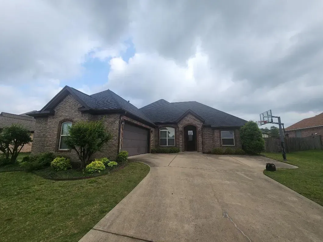 A large brick house with a black roof and a driveway leading to it.