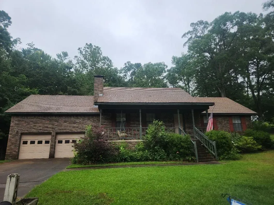 A house with a porch and a garage is surrounded by trees on a cloudy day.