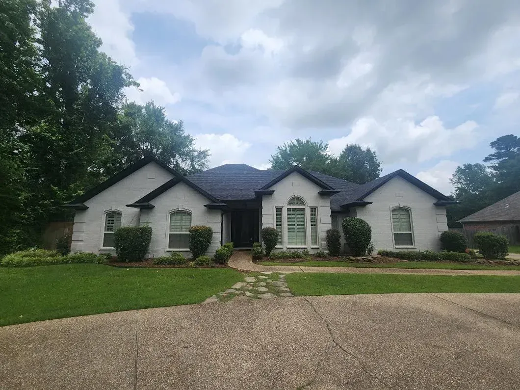 A large white house with a black roof is sitting on top of a lush green lawn.