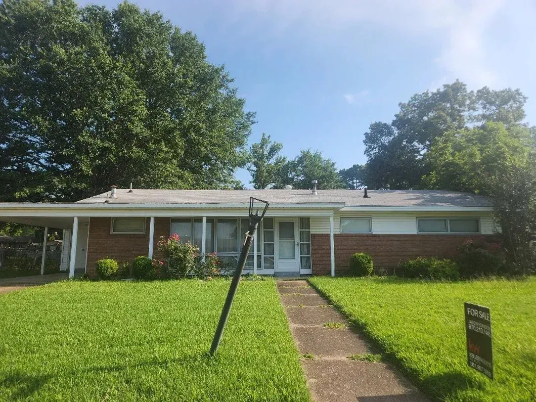 A brick house with a white porch and a for sale sign in front of it.