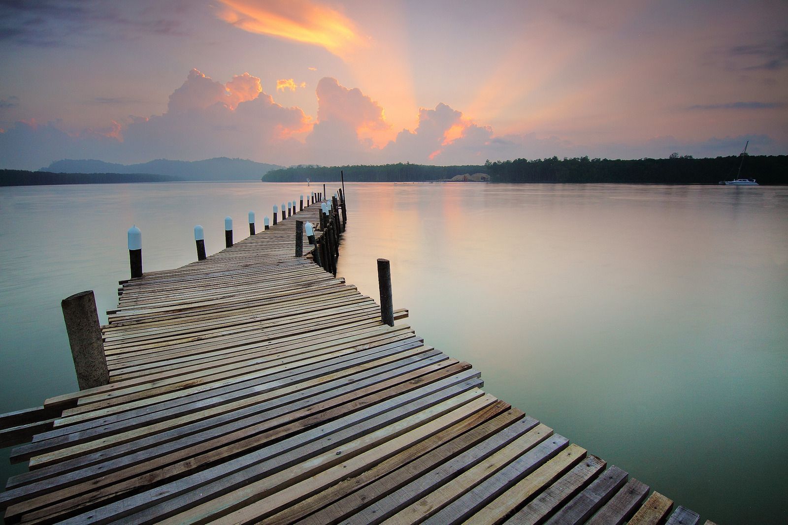 A wooden pier leading into a body of water at sunset.