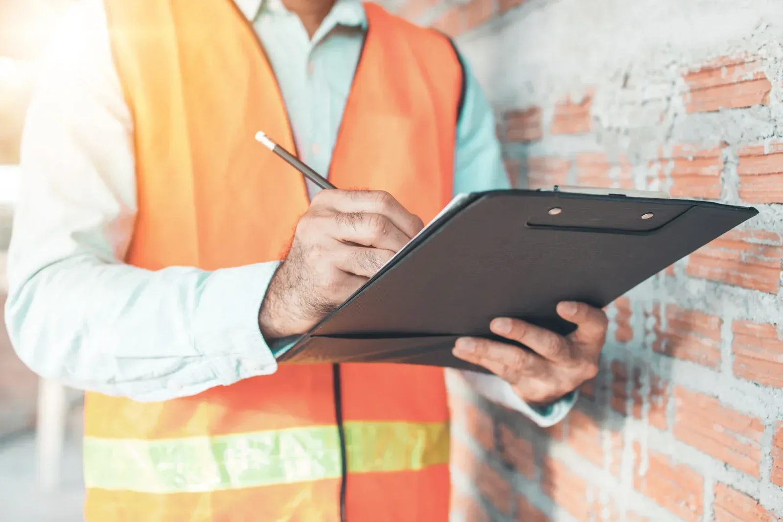 A construction worker is holding a clipboard and writing on it.