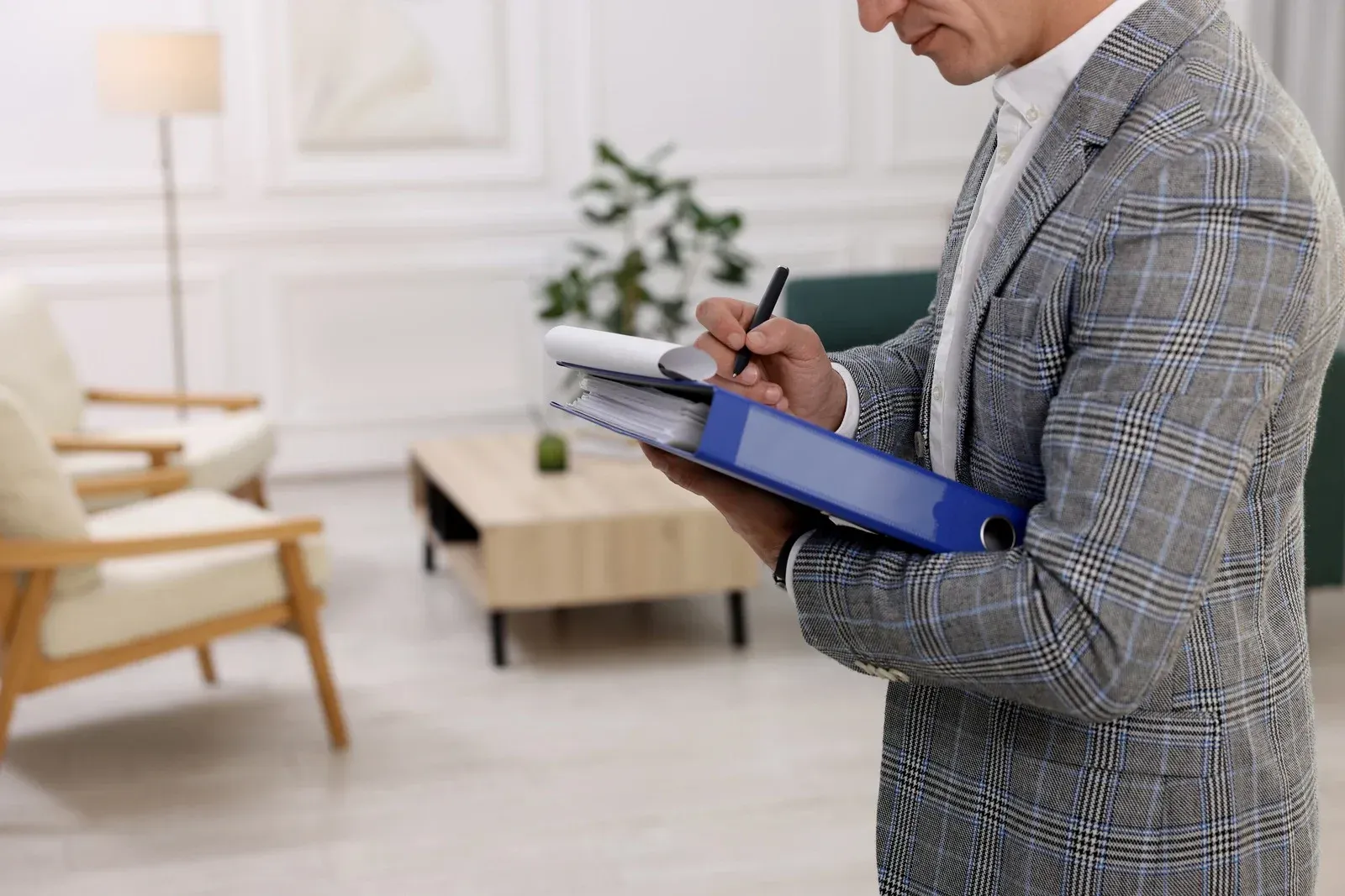 A man in a suit is writing on a clipboard in a living room.