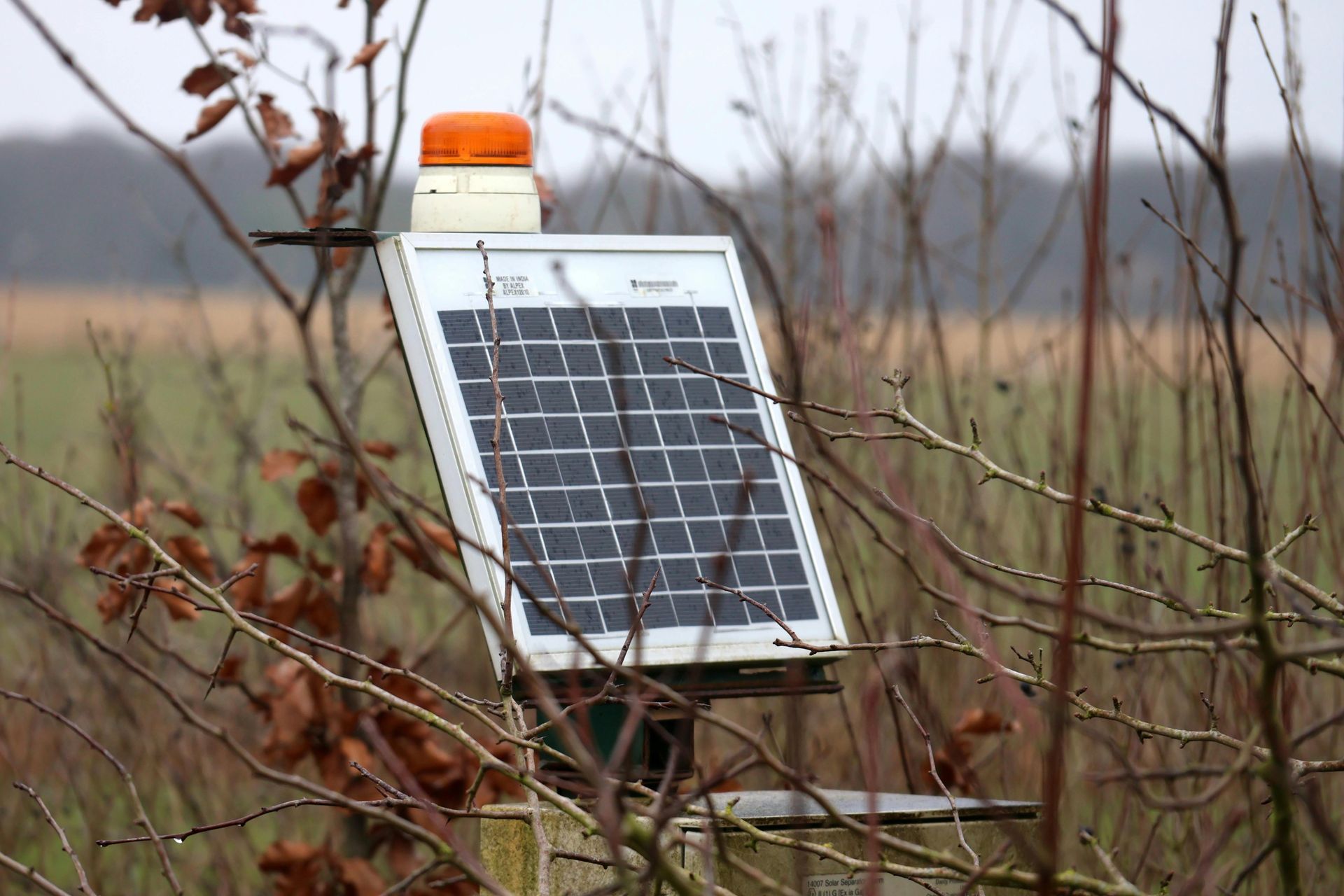 A small solar panel is attached to a pole in a field