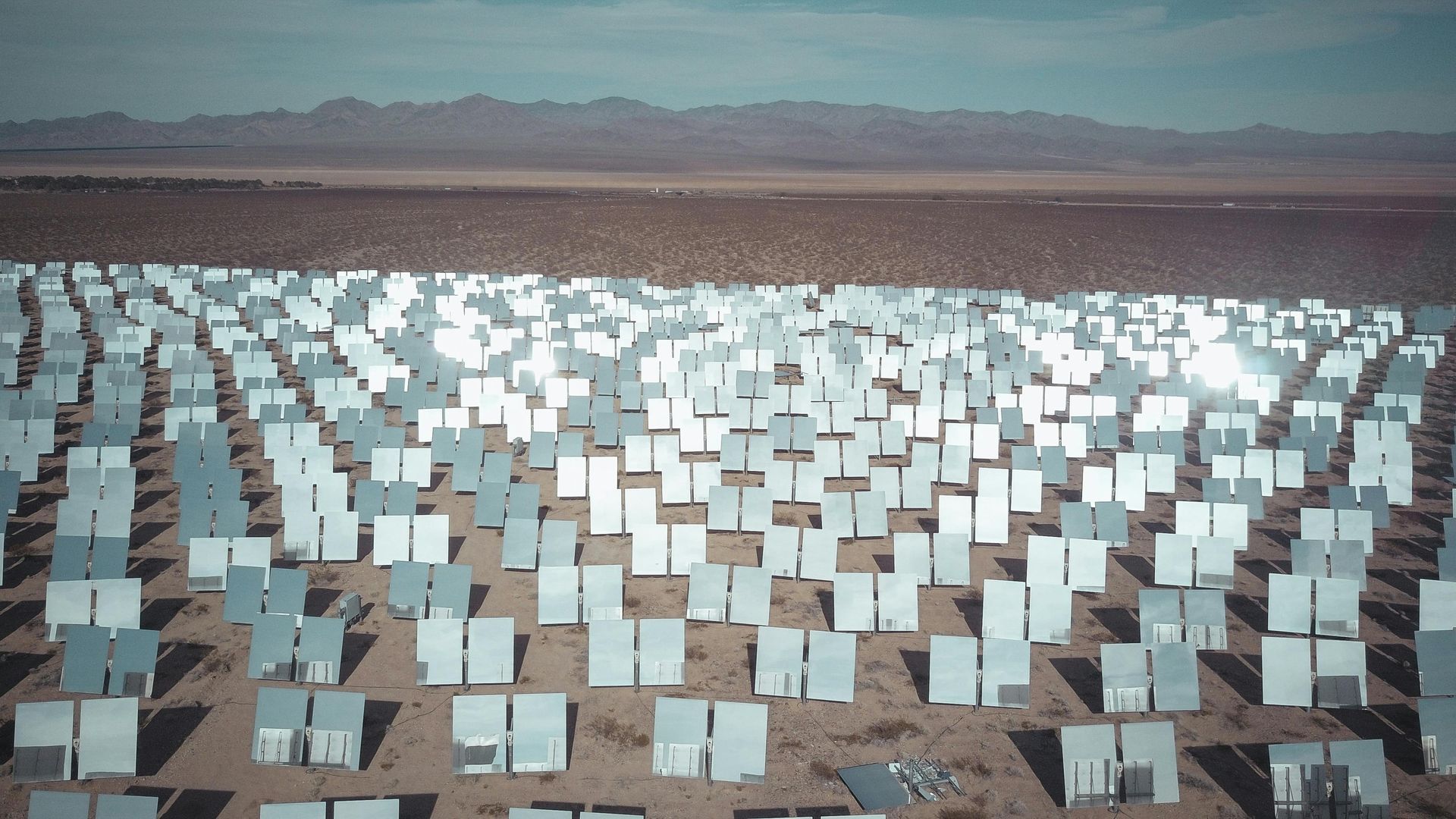 A large field of mirrors in the desert with mountains in the background