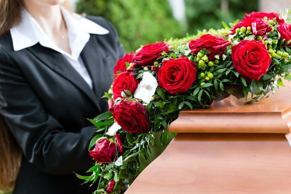 Una donna in abito nero depone una composizione floreale di rose rosse su una bara di legno all'aperto.