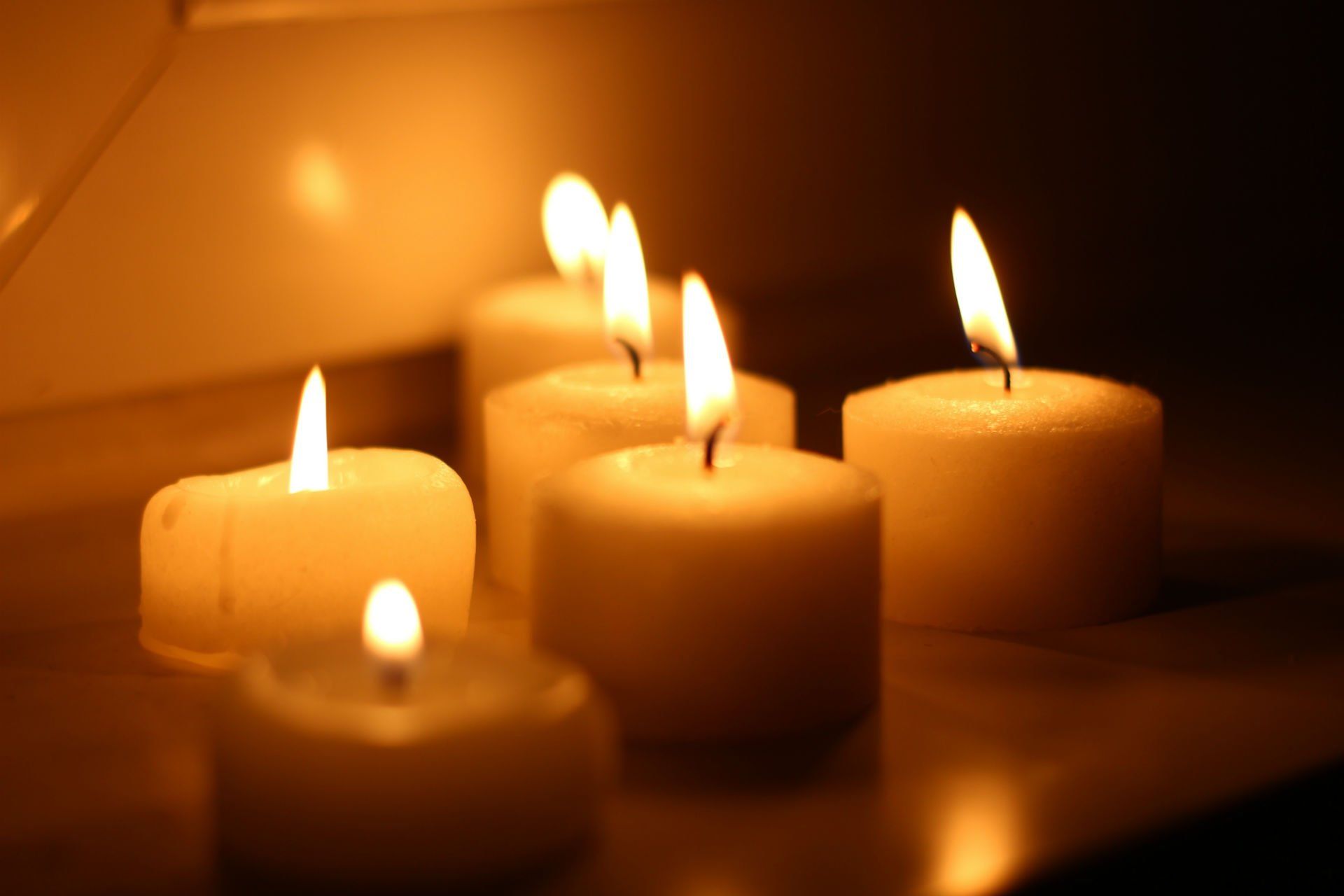 Candele bianche accese in una stanza buia, con le fiamme che proiettano una luce calda.