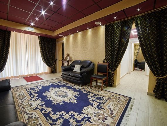 Una stanza con un tappeto a motivi blu e beige, divani in pelle nera, tende dorate e un soffitto rosso.