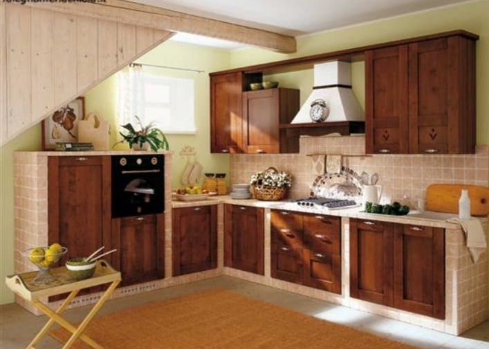 Una cucina rustica con mobili in legno, ripiani piastrellati, un forno nero e una cappa bianca sotto un soffitto inclinato.