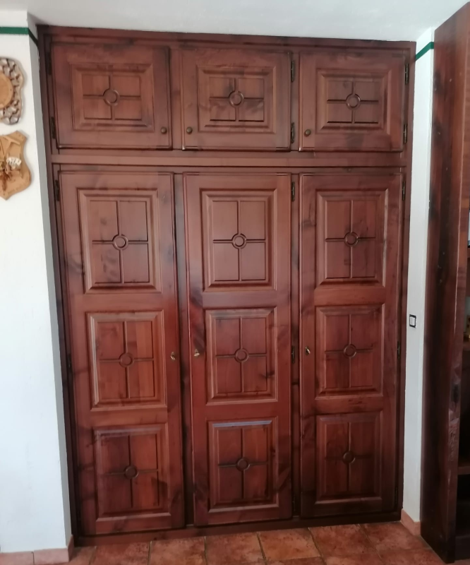 Un grande armadio in legno scuro con tre ante verticali dotate di pannelli a motivi quadrati incrociati e vani portaoggetti superiori.