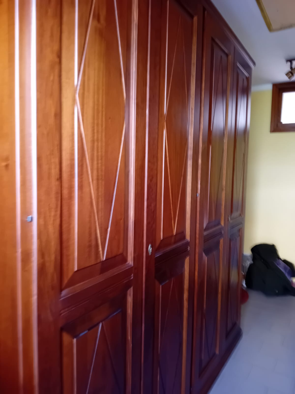 In una stanza dalle pareti gialle, una fila di armadi in legno lucido con intagli a forma di diamante sulle ante.