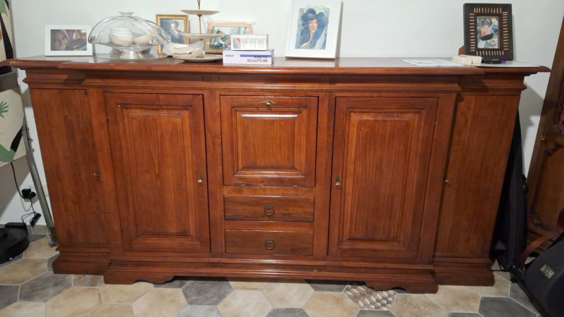 Una grande credenza in legno con quattro ante, due cassetti centrali e cornici decorative su un pavimento piastrellato.