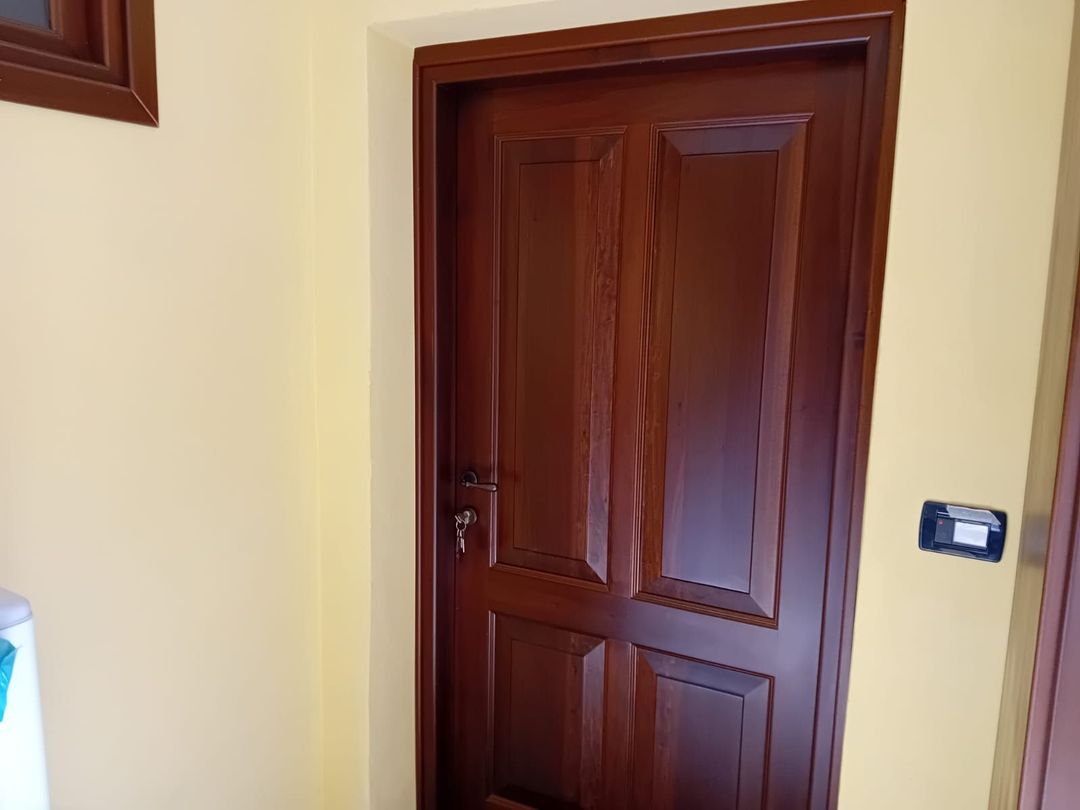 Un ingresso luminoso con una porta d'ingresso bianca affiancata da finestre laterali, caratterizzate da due porte in legno sulle pareti laterali.