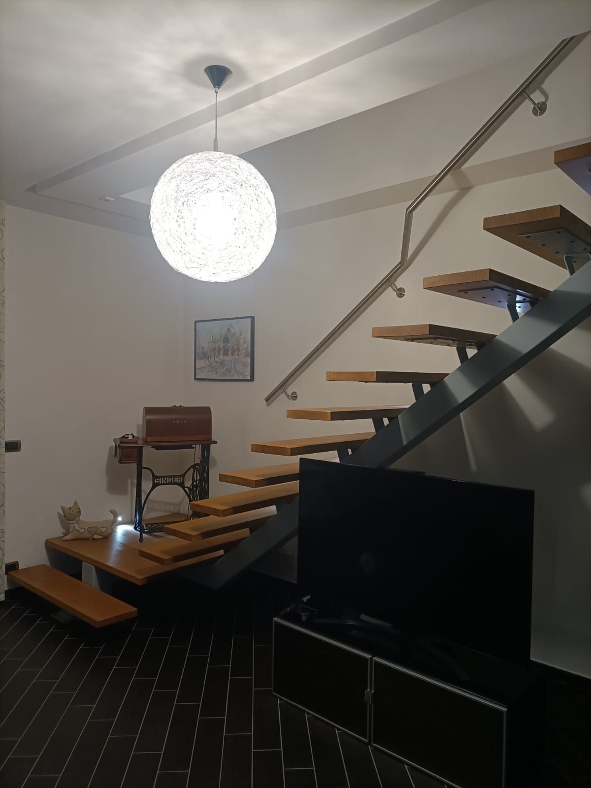 Una vista dall'alto di una scala in legno lucido con ringhiere decorative che scende curvando verso un corridoio piastrellato.