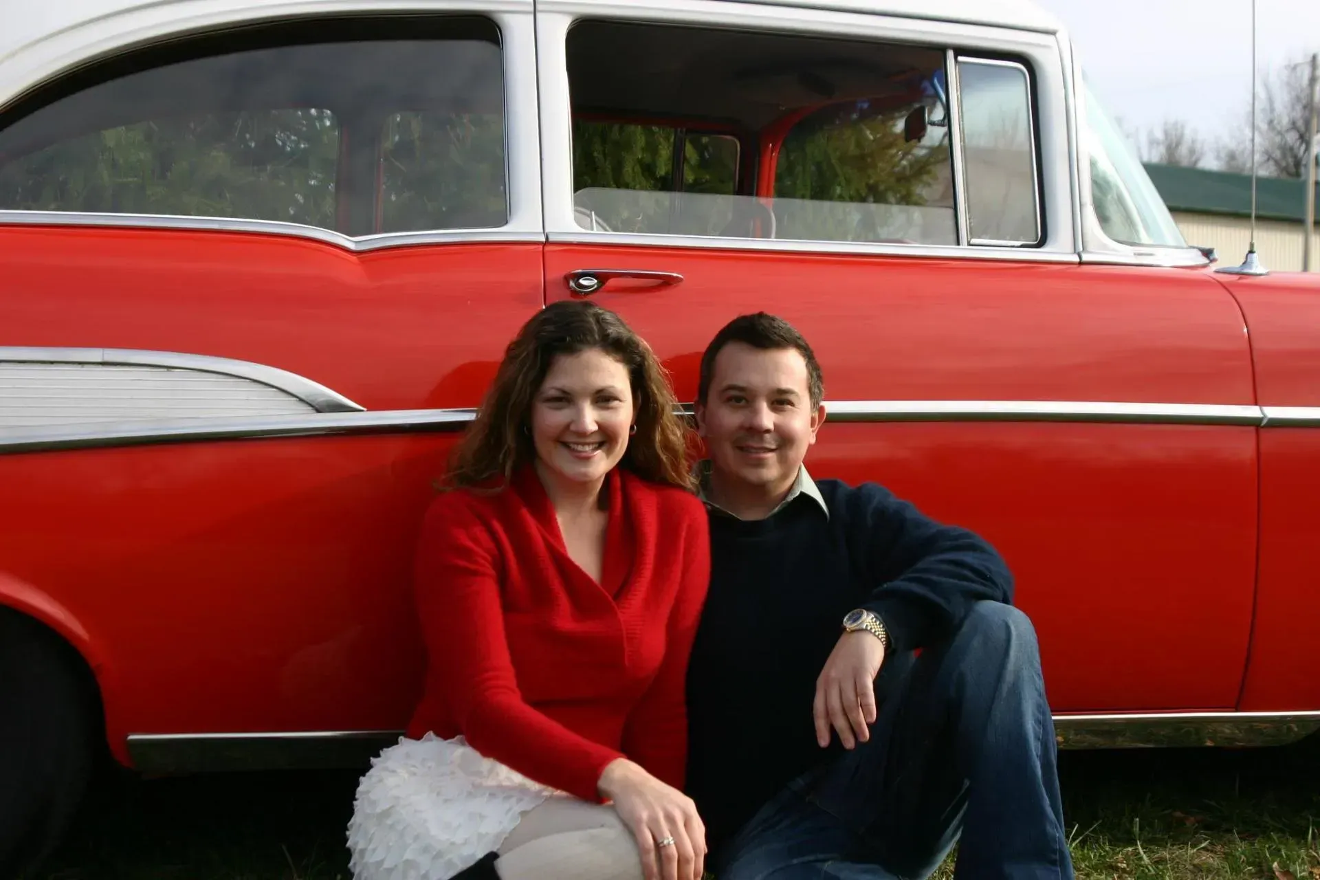 A man and a woman are posing for a picture in front of a red car