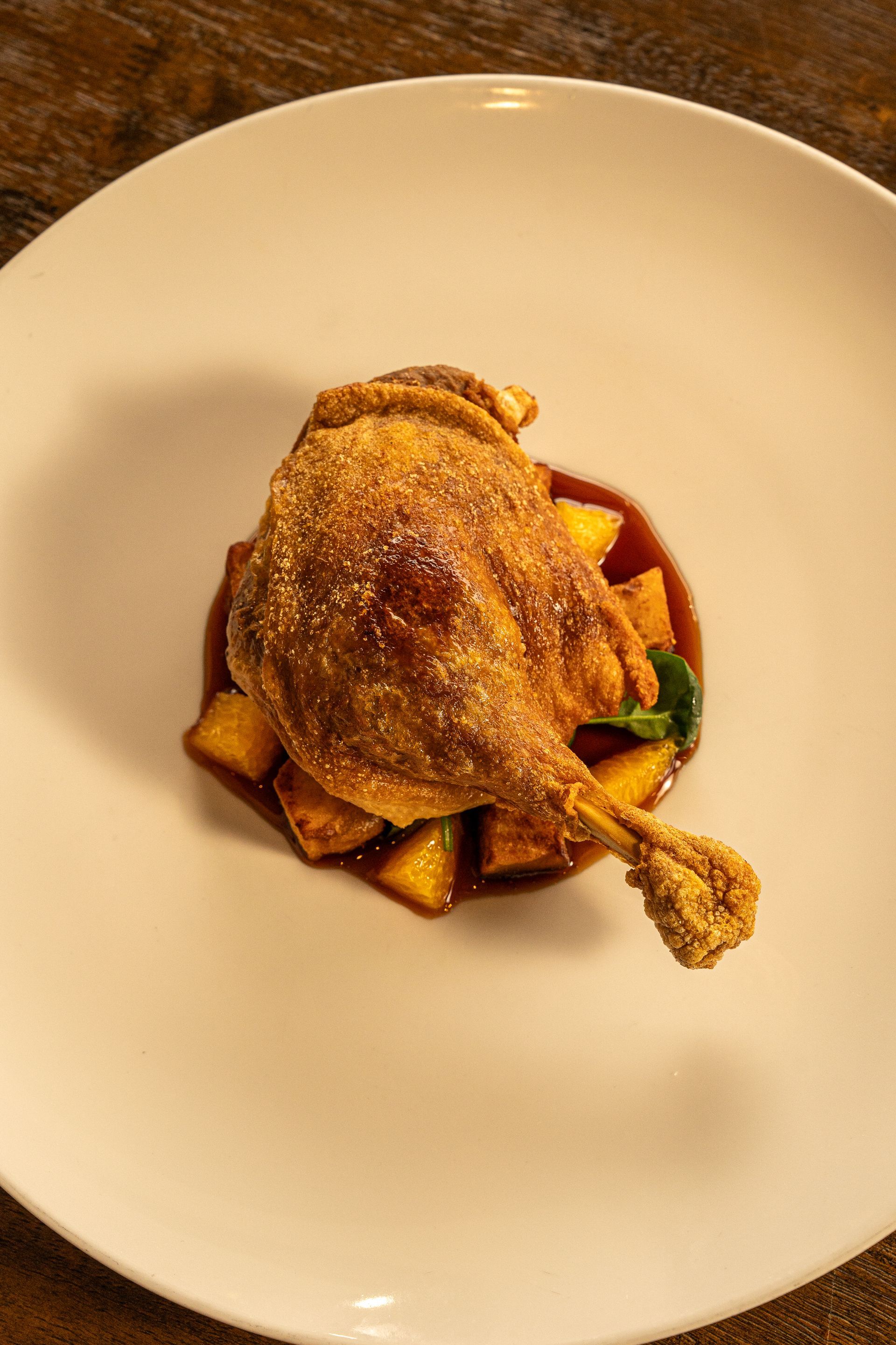 Crispy golden duck confit on bed of potatoes and sauce on a white plate.