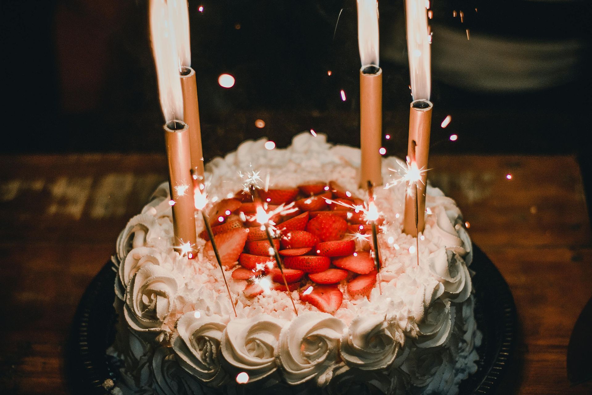 Birthday cake with sparkler candles and sliced strawberries.
