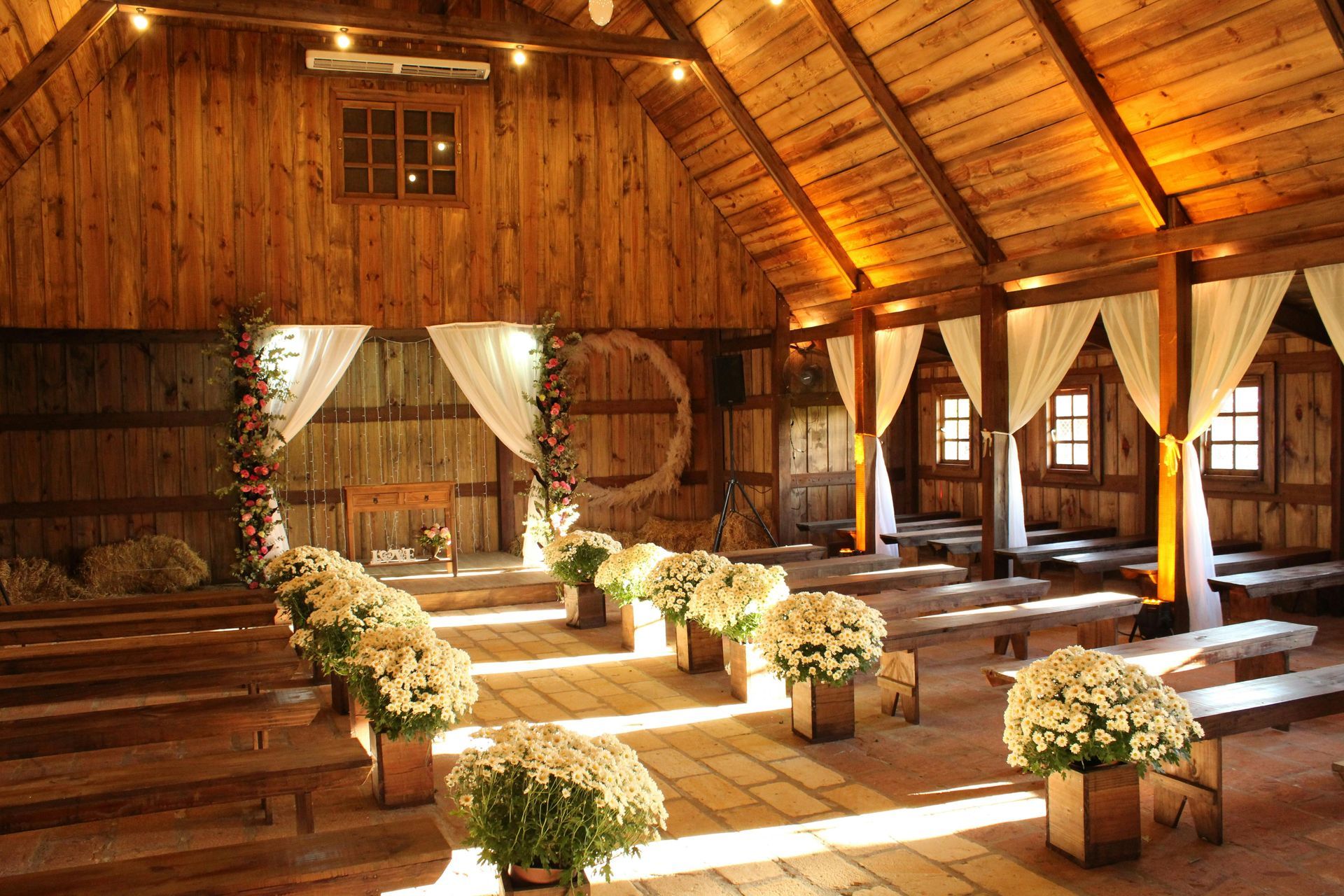 Rustic barn wedding setup with floral aisle and draped windows.