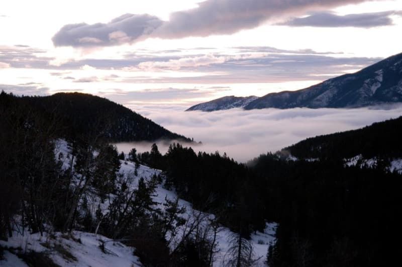 A snowy landscape with mountains and clouds in the background