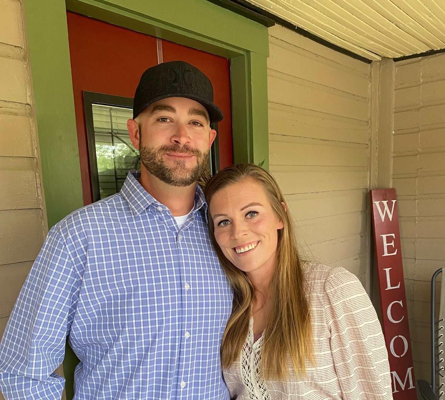 A man and woman are posing for a picture in front of a welcome sign