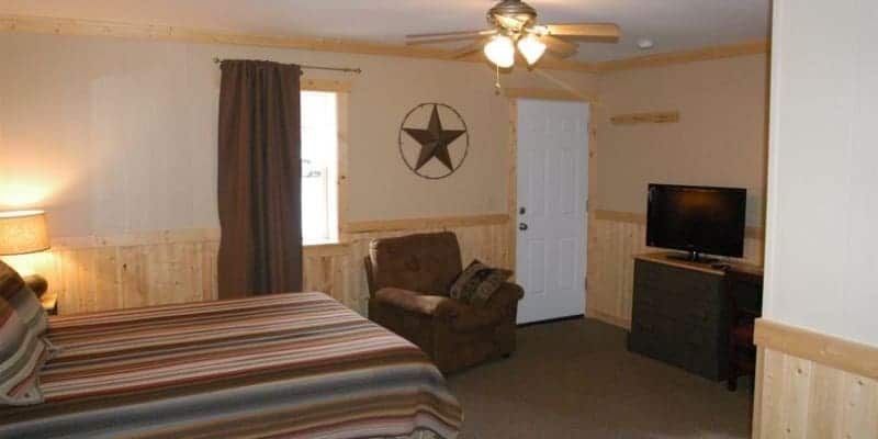 A hotel room with a bed , chair , television and a ceiling fan.