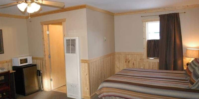 A bedroom with a bed , a refrigerator , a microwave and a ceiling fan.