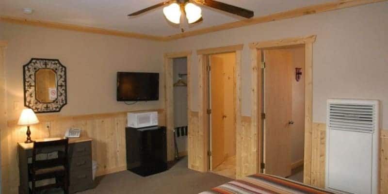 A hotel room with a bed , desk , television and ceiling fan.