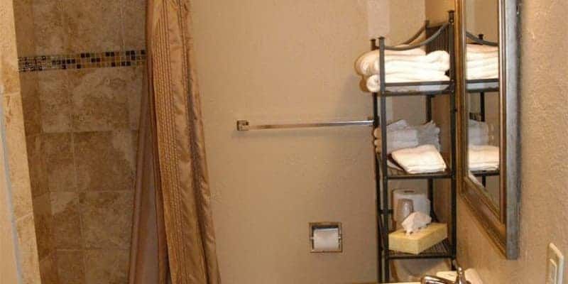 A bathroom with a shower , sink , mirror and towel rack.