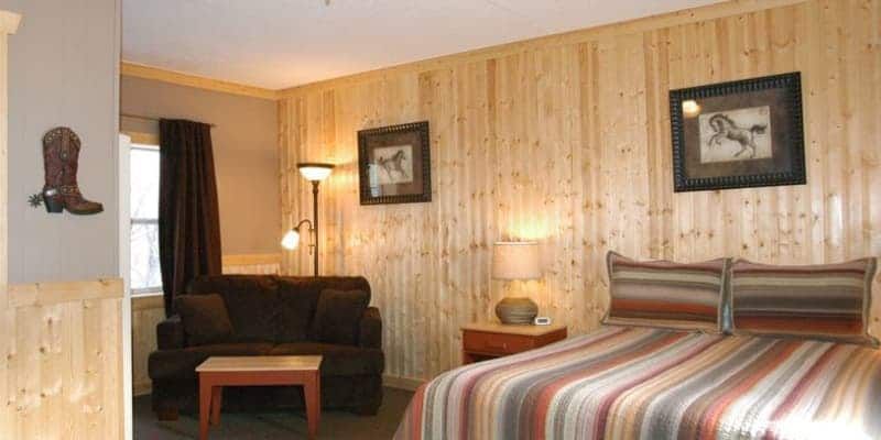 A bedroom with a bed , couch , table and cowboy boots on the wall.